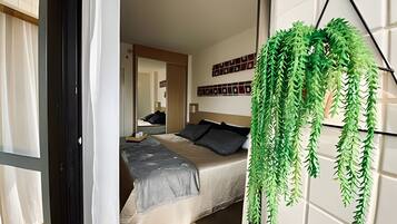 Un dormitorio con cama, mesita de noche, planta colgante y un muro con cuadros.