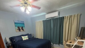 A bedroom with a bed, a desk, an air conditioning unit, a ceiling fan, and a painting on the wall. - The Blue Palace (Tampa)