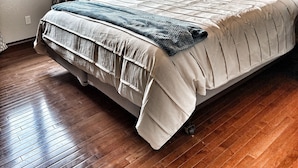 A bedroom with a large bed, wooden flooring, a window with curtains, and a painting on the wall.