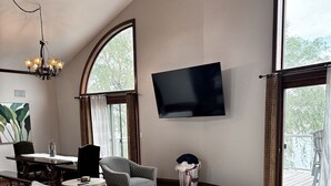 A living room with a ceiling fan, a flat-screen TV, a sofa, a dining table with chairs, and large windows.