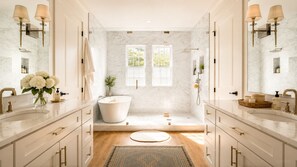 Een ruime badkamer met twee wastafels, een bad en een groot raam.
