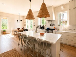 Una cocina amplia con una isla grande, muebles blancos y lámparas colgantes de mimbre.