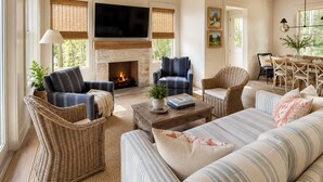 A living room with a fireplace, a television, wicker furniture, and a dining area. - Rabbit Ridge New Designer Cottage Screened Porch + Wood Fireplace | EV Charger (Cashiers)