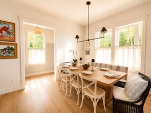 Ein Essbereich mit einem Holztisch, weißen Stühlen und einer Bank. Zwei Pendelleuchten hängen über dem Tisch.