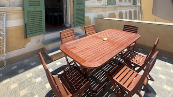 A building with a balcony, a wooden table, and green shutters.
