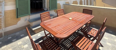 A building with a balcony, a wooden table, and green shutters.