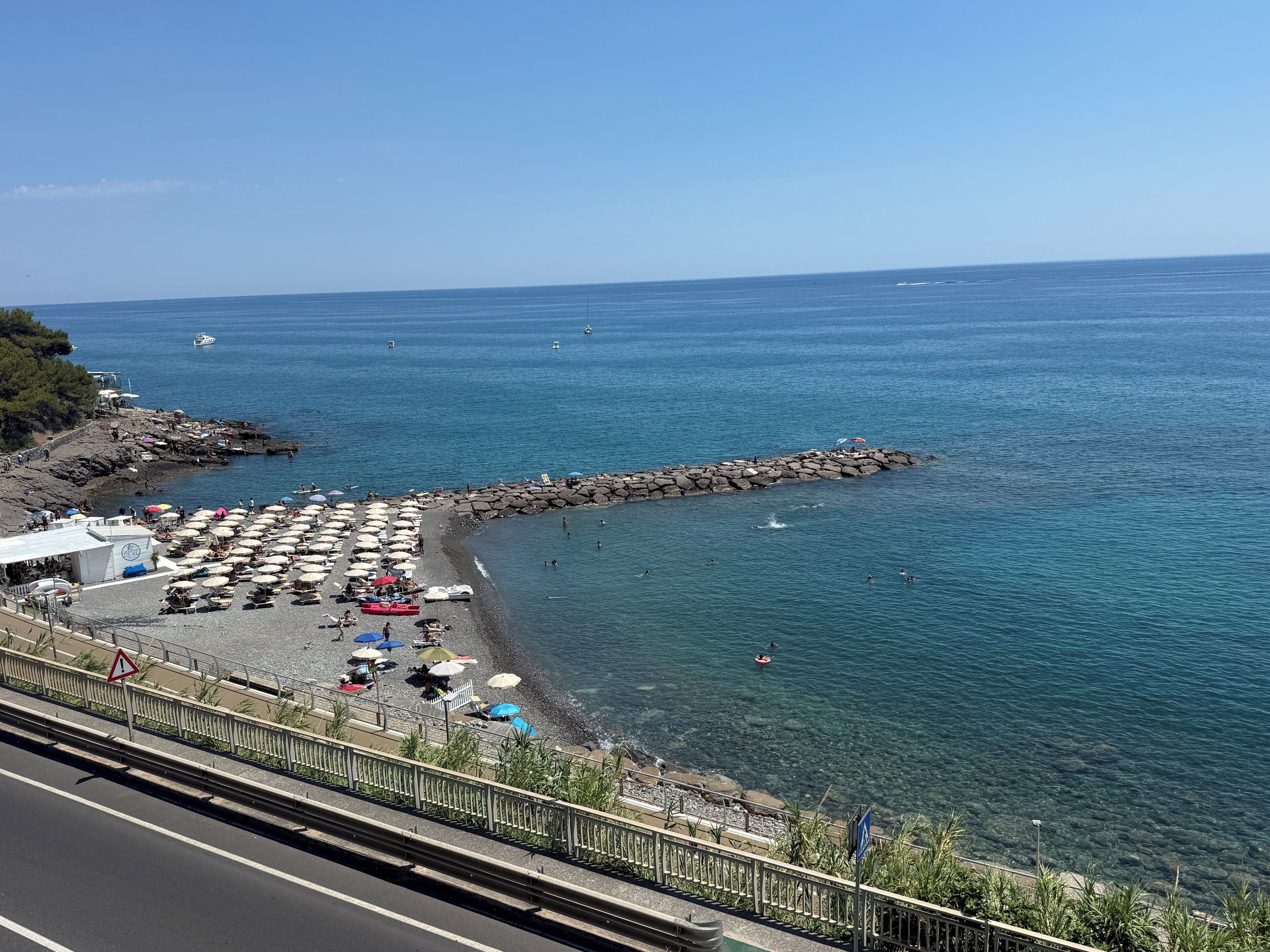 A coastal beach with umbrellas, a rocky breakwater, and a clear view of the sea.