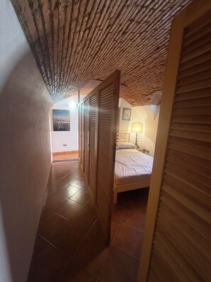 Un pasillo estrecho con techo inclinado que da a un dormitorio con cama y mesita de noche.