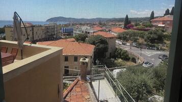 A view through a window with a mesh screen, featuring a building with a red roof, a parking area, and a clear sky.