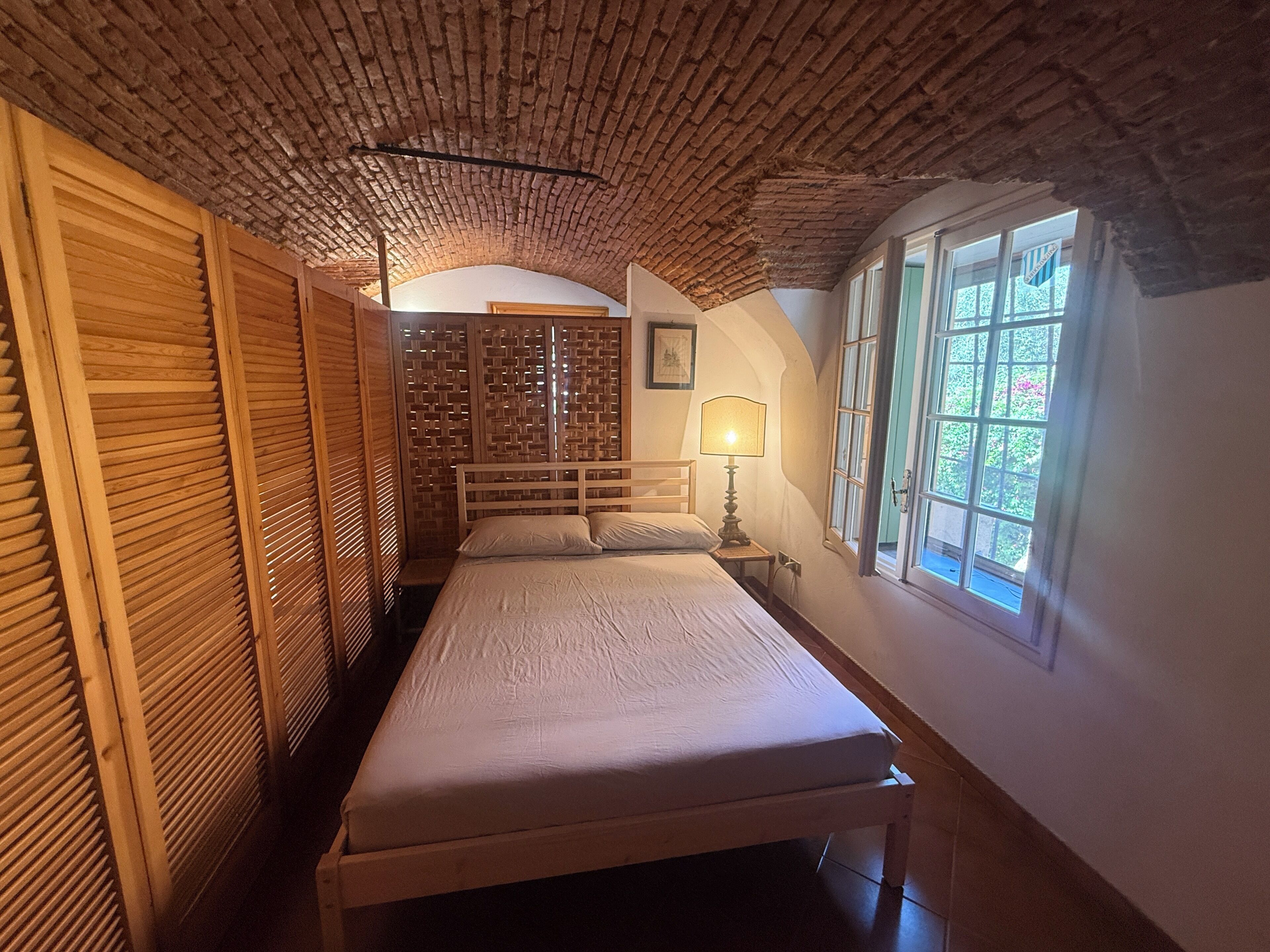 A room with a bed, a window, and a wooden ceiling.