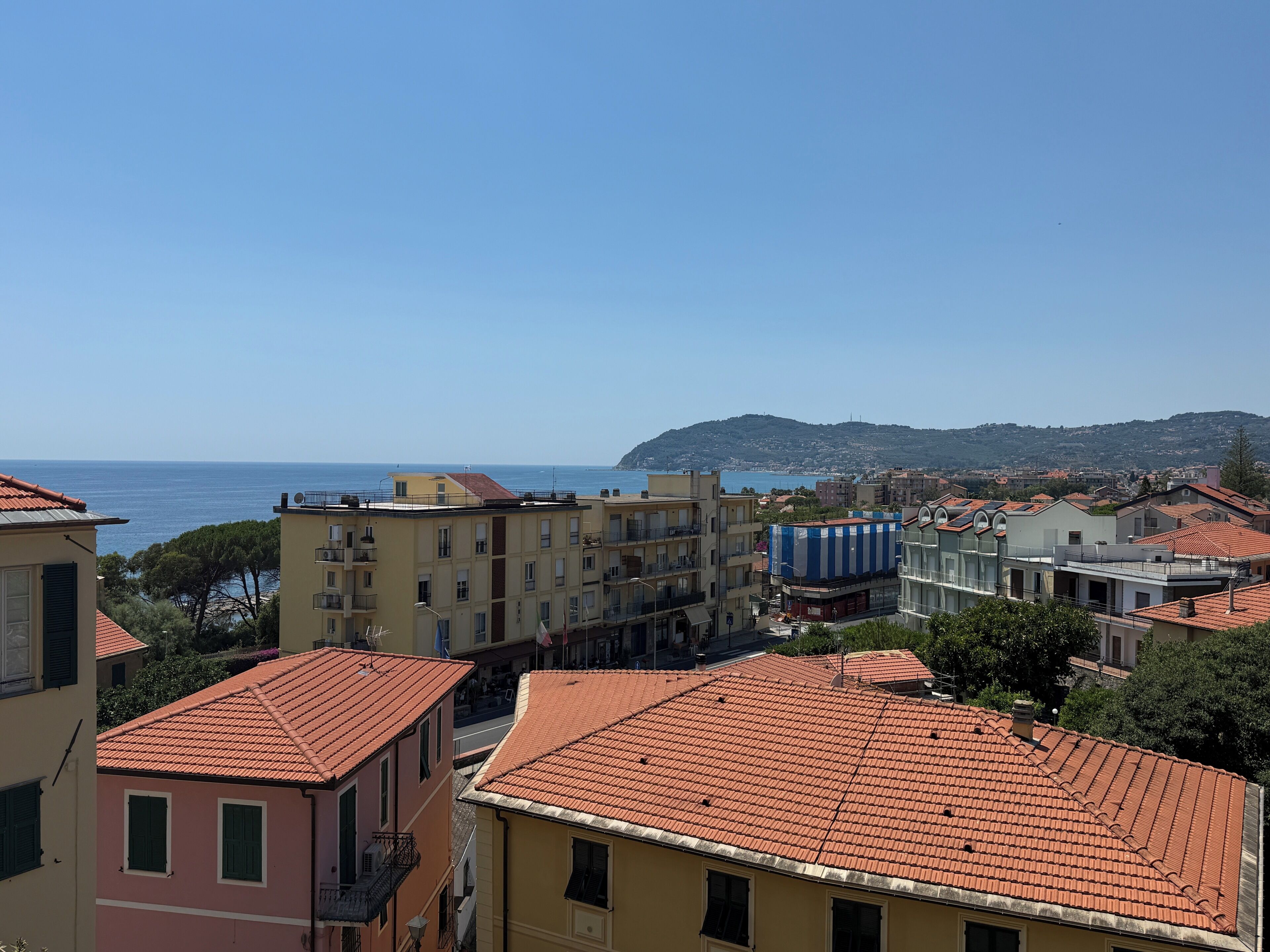 Une ville côtière aux bâtiments aux toits de tuiles rouges, avec un ciel dégagé et une vue sur la mer.