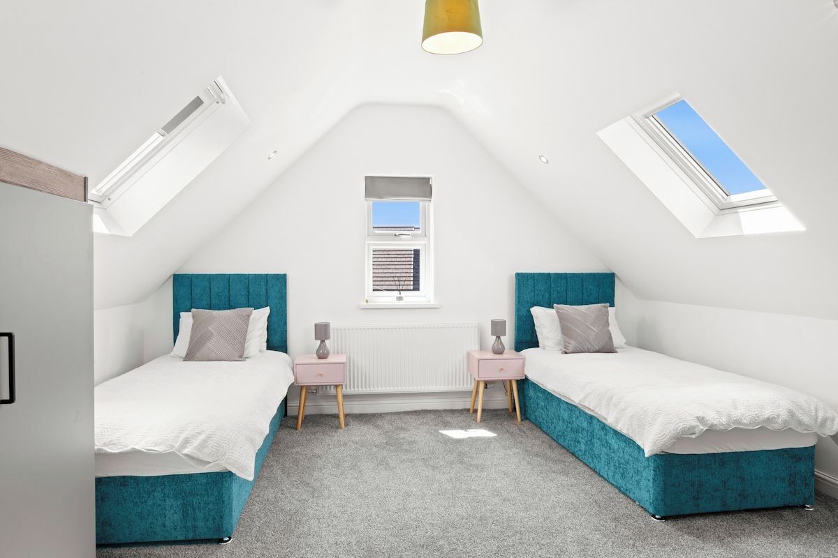Een slaapkamer met twee bedden, een dakvenster, een raam en een radiator.