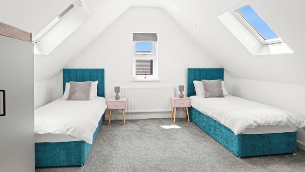 A bedroom with two beds, a skylight, a window, and a radiator.