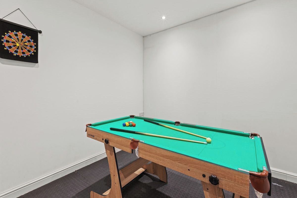 Een pooltafel met ballen en stokken, een dartbord, en een kleine basketbal.