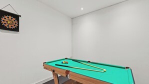 A pool table with balls and cues, a dartboard, and a small basketball.