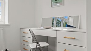 A white desk with drawers and a chair, a window, and a framed picture on the wall.