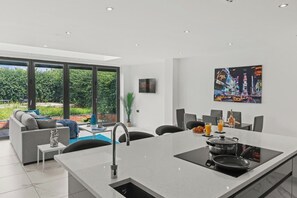 Eine moderne Küche mit Kochinsel, ein Essbereich mit Ausblick und ein Wohnbereich mit Sofa und Couchtisch.
