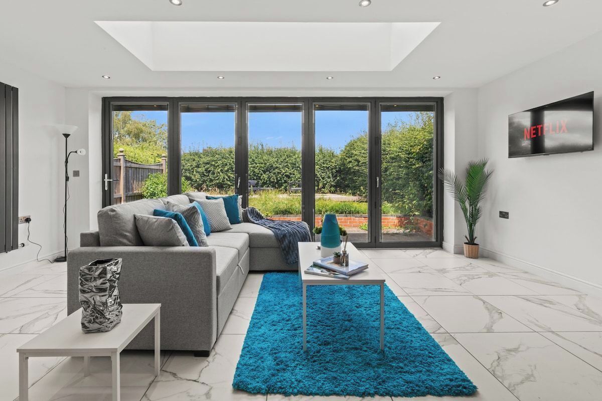 Een moderne woonkamer met een grijze bank, een blauw vloerkleed en een televisie aan de muur.