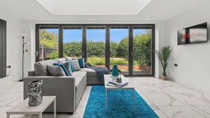 A modern living room with a grey sofa, a blue rug, and a TV on the wall.