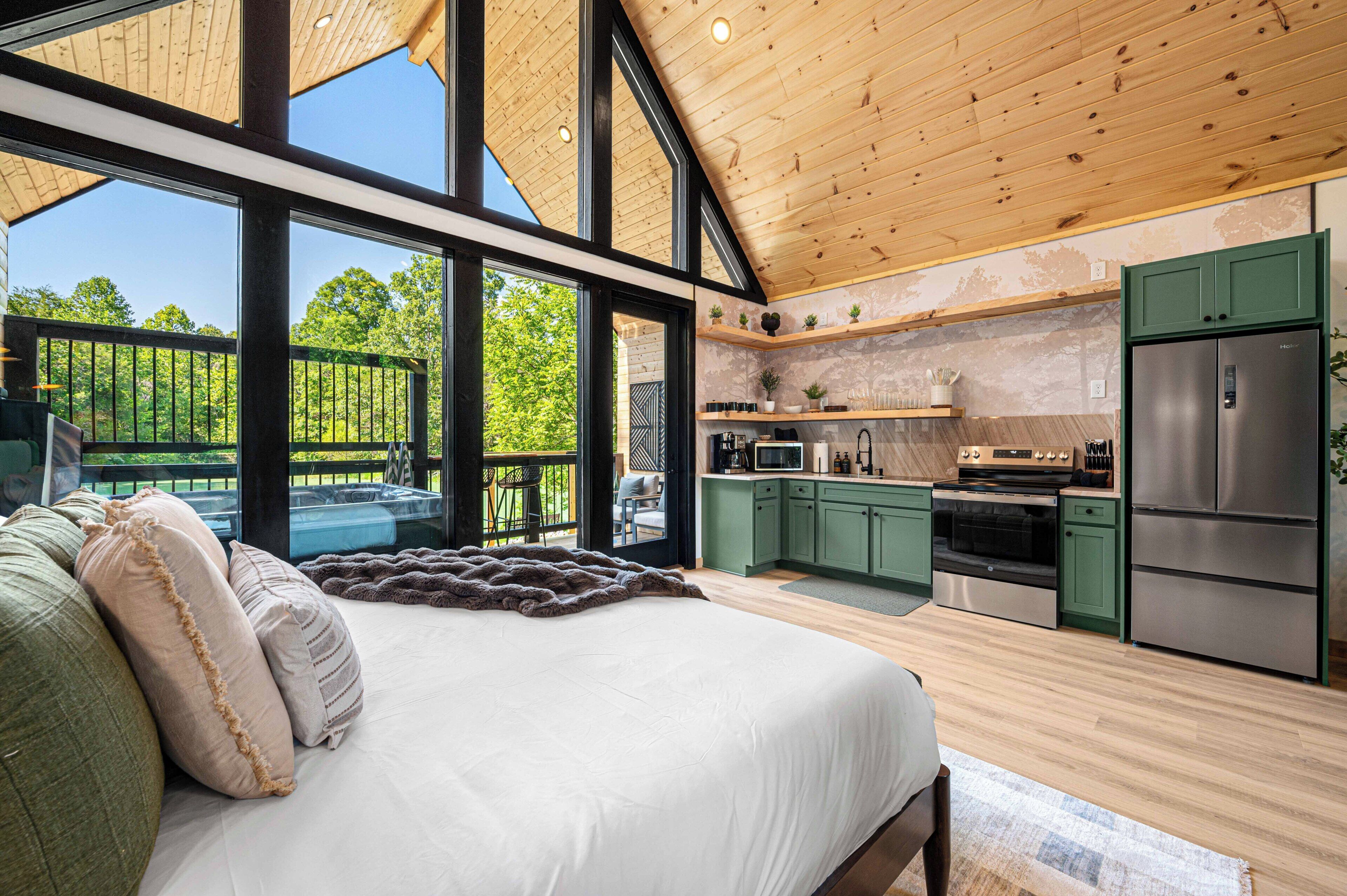 Un dormitorio moderno con una cama grande, vistas al exterior y una cocina con armarios verdes y electrodomésticos de acero inoxidable.