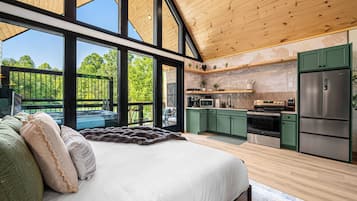 Un dormitorio moderno con una cama grande, vistas al exterior y una cocina con armarios verdes y electrodomésticos de acero inoxidable.