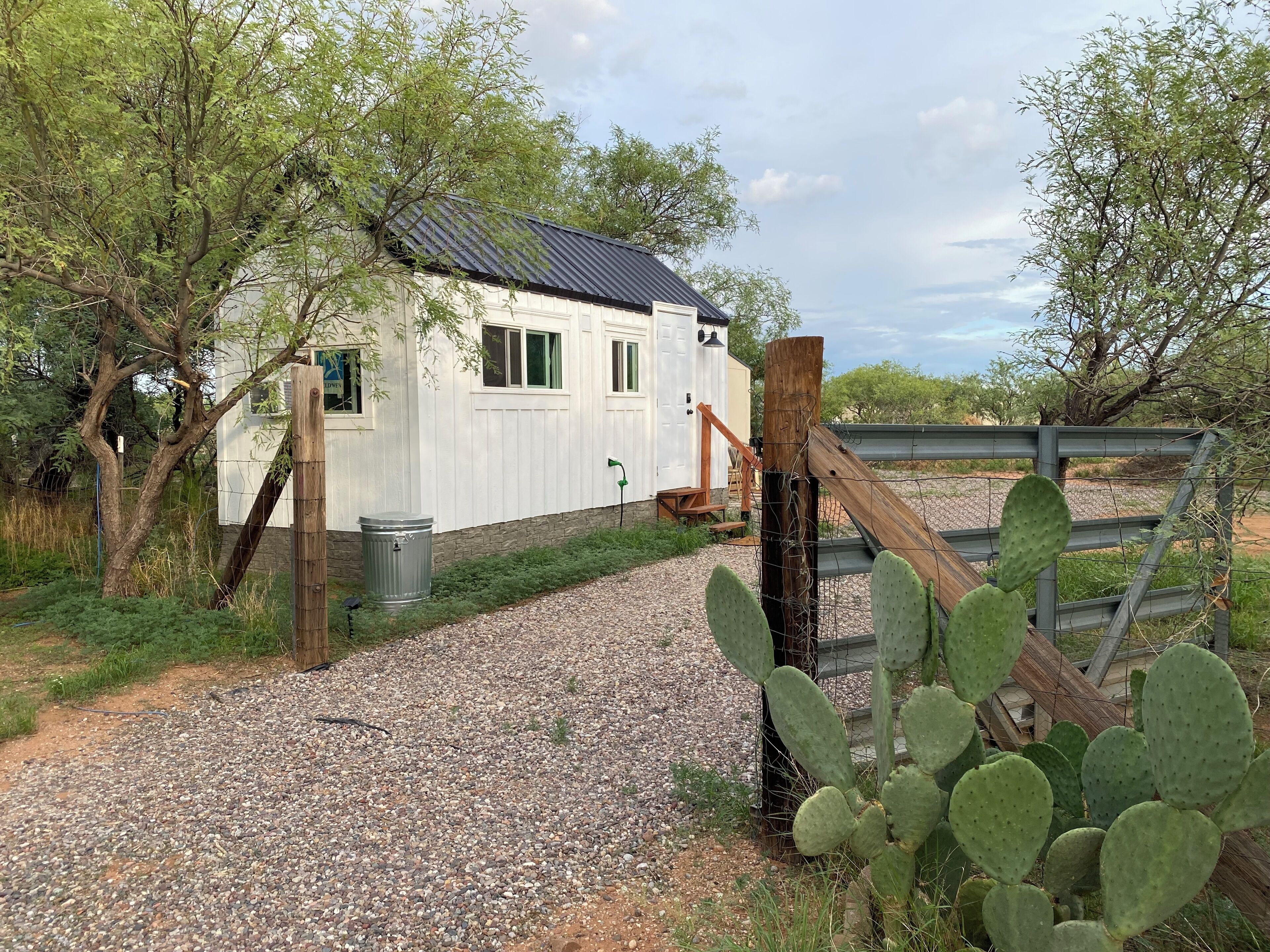 A white building with a metal roof, a gravel path, and a wooden fence.