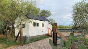 A white building with a metal roof, a gravel path, and a wooden fence. - Board and batten single unit #1 (Sierra Vista)