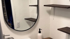 A bathroom with a white sink, a mirror, a toilet, and wooden shelves. - Board and batten single unit #1 (Sierra Vista)