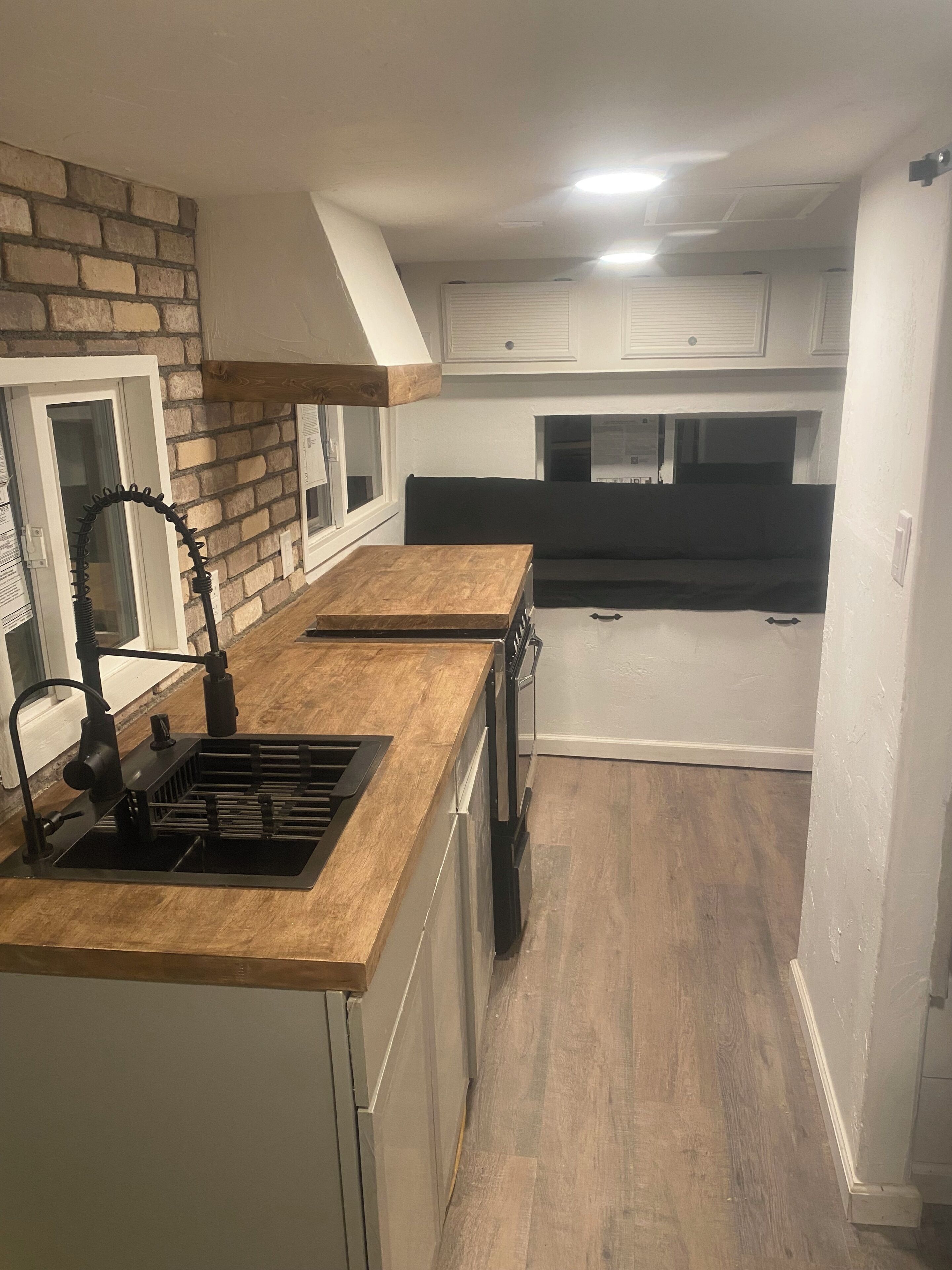 Una cocina compacta con cubierta de madera, pileta integrada y alacenas blancas.