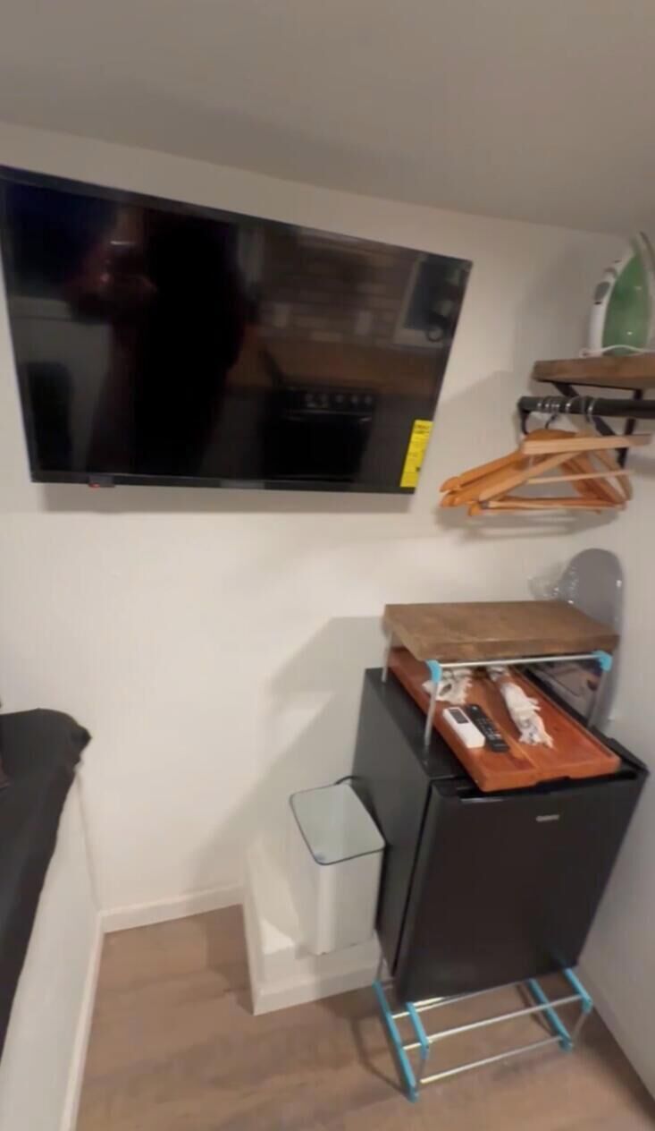 Ein Zimmer mit einem an der Wand befestigten Flachbildfernseher, einem kleinen Tisch mit Tablett und einem schwarzen Schrank mit Tablett darauf.