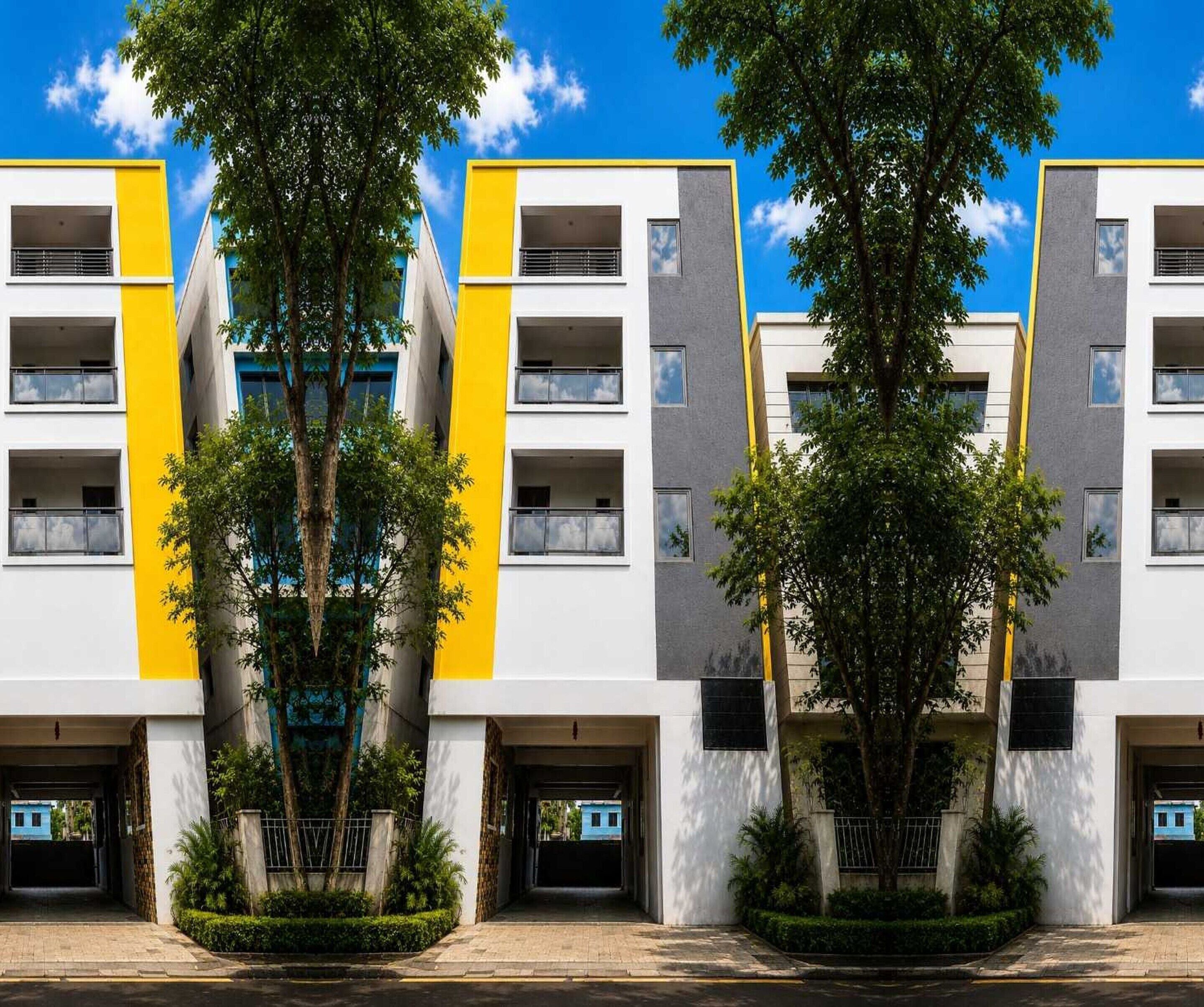 A multi-story building with balconies, a central entrance, and surrounding greenery.