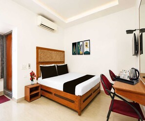 Ein Hotelzimmer mit einem hölzernen Bett, einem Schreibtisch mit Stuhl, einer Klimaanlage und einem Kunstwerk an der Wand.