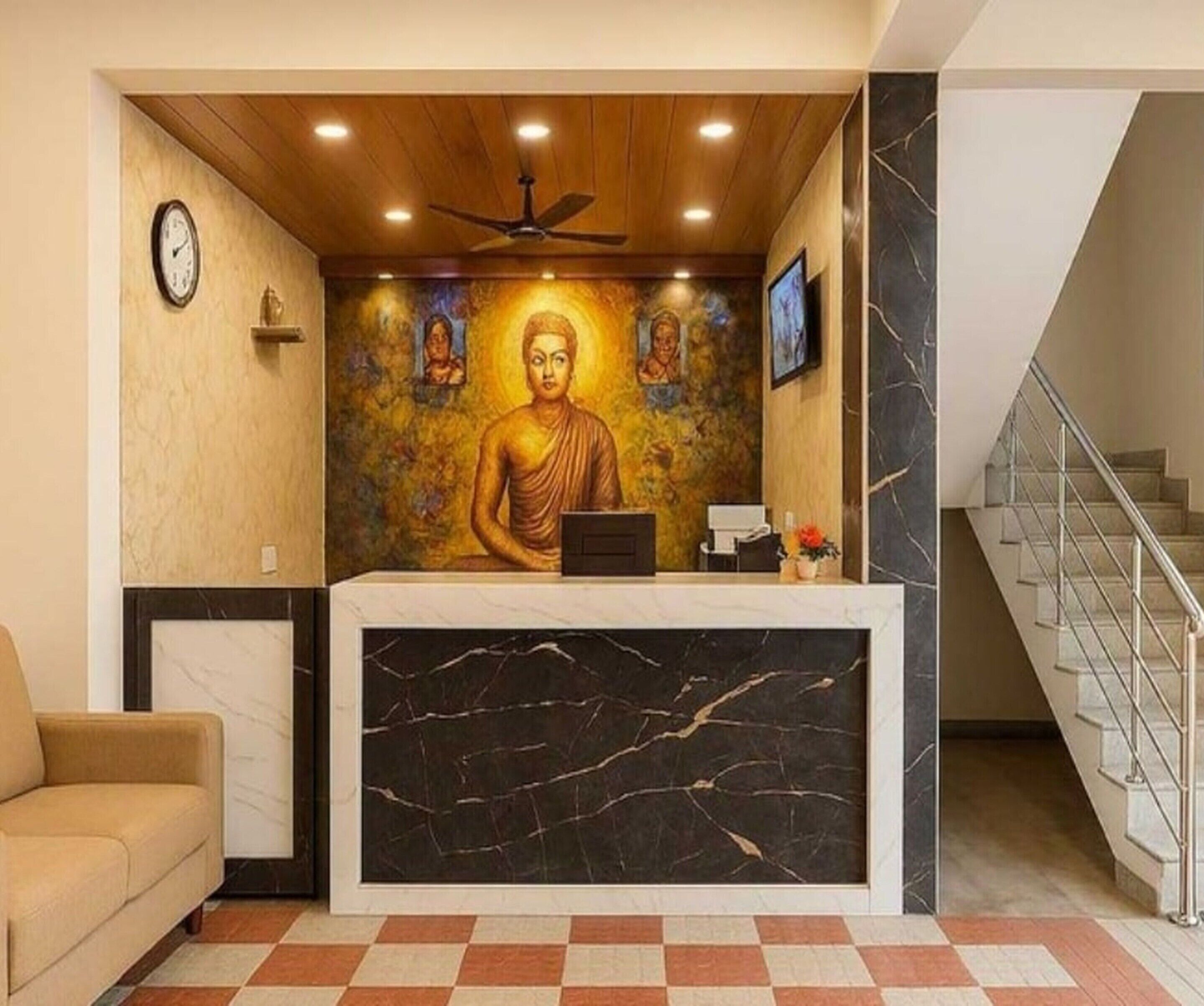 Uma área de recepção com uma estátua de Buda, um relógio, um ventilador de teto e uma escadaria.