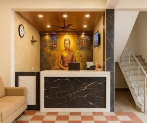 Ein Empfangsbereich mit Buddha-Statue, einer Uhr, einem Deckenventilator und einer Treppe.