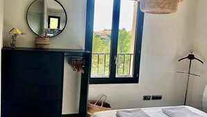 A bedroom with a bed, a dresser, a mirror, a window with a view, and a hanging light fixture. - Villa de La Verdière, perfect for families (La Verdière)