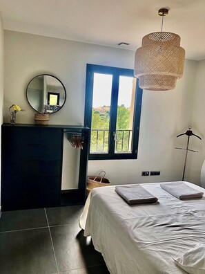 A bedroom with a bed, a dresser, a mirror, a window with a view, and a hanging light fixture. - Villa de La Verdière, perfect for families (La Verdière)