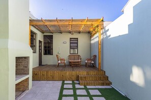 A covered patio with a wooden deck, two wicker chairs, and a small table.