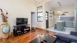 Una sala de estar con televisor, una mesa de centro y un sofá. Hay una zona de cocina con un lavamanos y armarios.