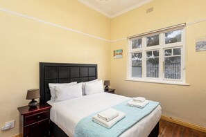A hotel room with a bed, two bedside tables, a window, and a painting on the wall.
