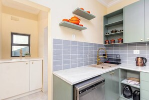 A kitchen with a dishwasher, a sink with a gold faucet, and shelves with kitchenware.