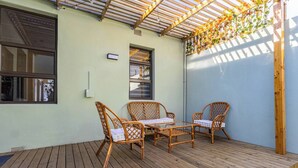 Un patio cubierto con piso de madera, muebles de mimbre y vista a la calle.