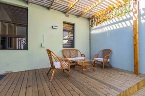 Un patio cubierto con piso de madera, muebles de mimbre y vista a la calle.