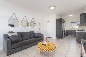 Ein modernes Wohnzimmer mit einem grauen Sofa, einem runden Couchtisch mit Holzplatte und drei Wandspiegeln.
