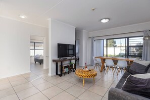 A modern living room with a flat-screen TV, a dining table with chairs, and a sofa. - Modern 3-bed Garden, Pool & gym by Ctha (Cape Town)