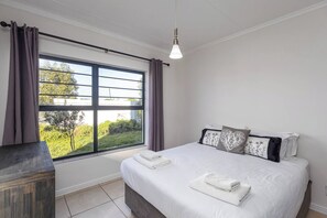 Ein Schlafzimmer mit großem Fenster, einem Bett mit weißer Bettwäsche und einem Nachttisch.