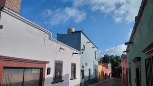 A narrow cobblestone street lined with colorful buildings, featuring a mix of architectural styles and a clear blue sky. - Casa Aldama 83. (San Miguel de Allende)