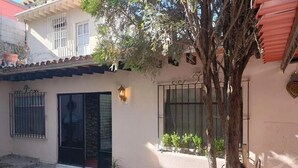A building with a white facade, a black door, and a window with a metal gate. - Casa Aldama 83. (San Miguel de Allende)
