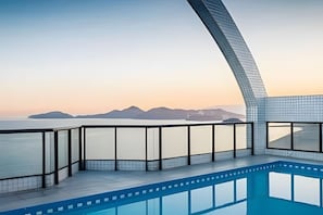 A modern pool area with a glass balustrade overlooking a body of water and distant mountains. - SHB Serenidade Marítima (Santos)
