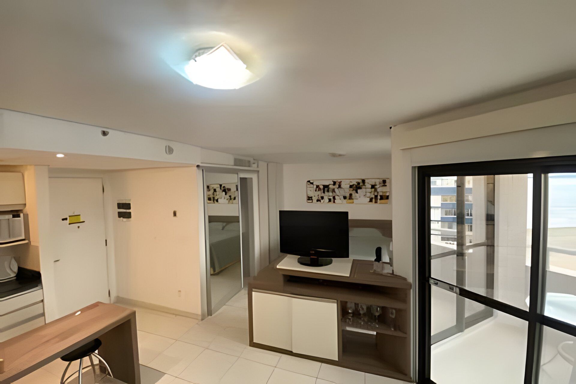 Una cocina moderna con un televisor de pantalla plana, una zona de comedor con una mesa de madera y un amplio ventanal corredero que da a un balcón.