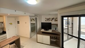 Eine moderne Küche mit Flachbildfernseher, einem Essbereich mit Holztisch und einer großen Glasschiebetür, die auf einen Balkon führt.